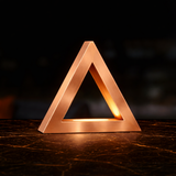 Copper finish triangular lamp by WOOM with a warm glow on a dark, veined marble table.